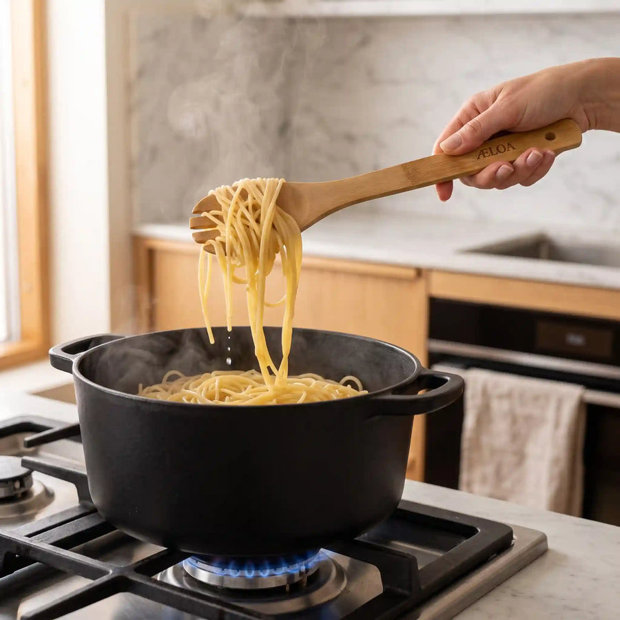 Hånd løfter spaghetti op af dampende gryde på gaskomfur med pastaske i bambus fra ÆLOA